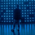 Person looking to the back of a stage which has hundreds of blue lights arranged in a grid